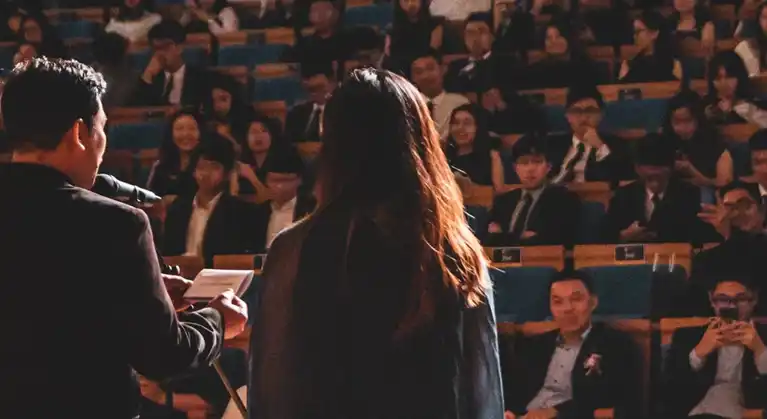 A man and woman's back faces the camera as they speak to an audience