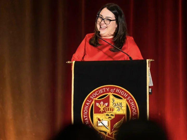 Woman speaking at podium with NSHSS Emblem