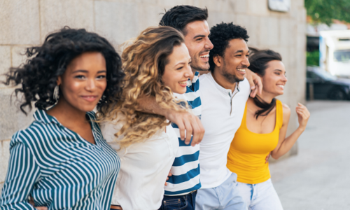 Group of diverse young adults walking arm in arm outdoors, smiling and enjoying time together
