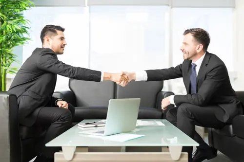 Two young men shaking hands wearing suits in the office