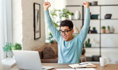 Student throws fists up in excitement over something he sees on a laptop screen