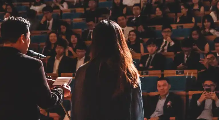 A man and woman's back faces the camera as they speak to an audience