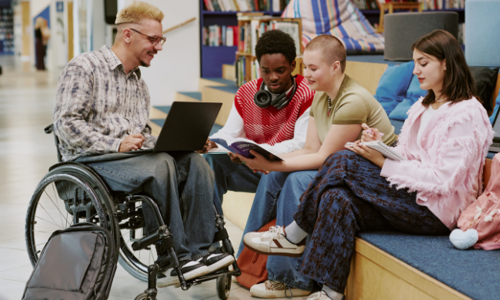 Group of students, including one in a wheelchair, gathered in a modern learning space, reading and discussing a book together in an inclusive and supportive environment