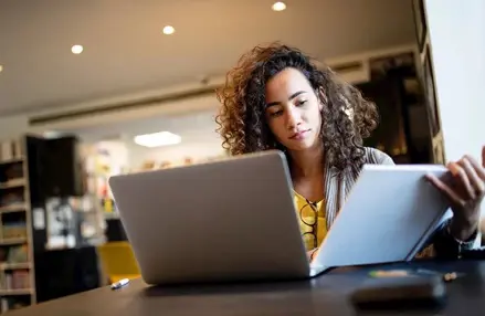 woman looking at notebook and laptop