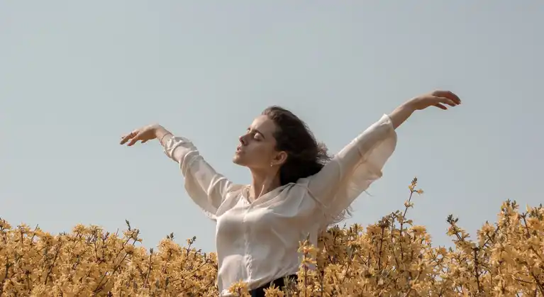 Woman raising her hands in the sky in the middle of a field