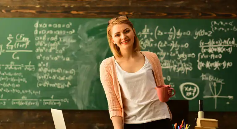 A teacher holding a cup of coffee in front of a chalkboard