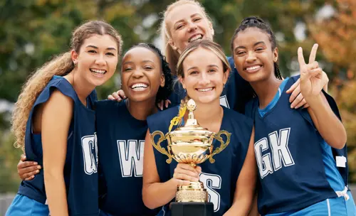 Girls' sports team posing proudly with a trophy, smiling and celebrating their achievement